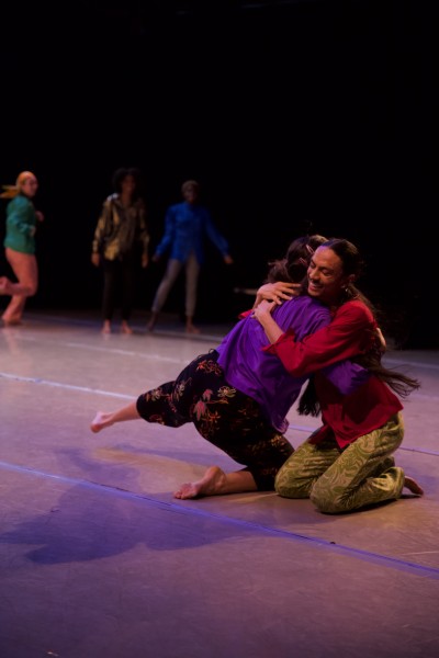 image of 2 performers embracing and smiling on the ground in bright, colorful clothing