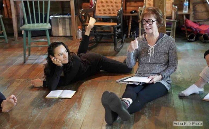 Two white women sitting on the floor with notebooks in hand discussing dance excitedly