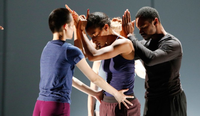 Four figures stand; two figures with their hands clasped, facing a third figure holding the hips of the front figure