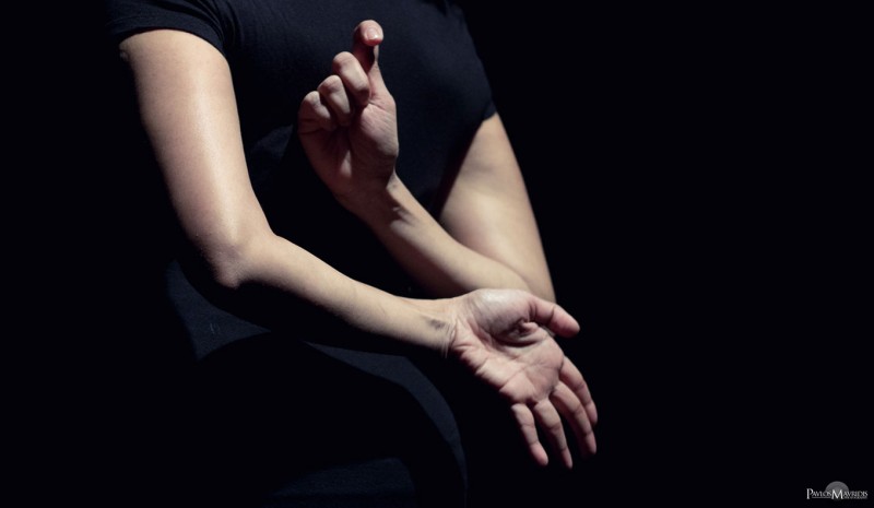 A person waring a dark t-shirt has their arms crossed behind their back and is holding two different shapes with their hands