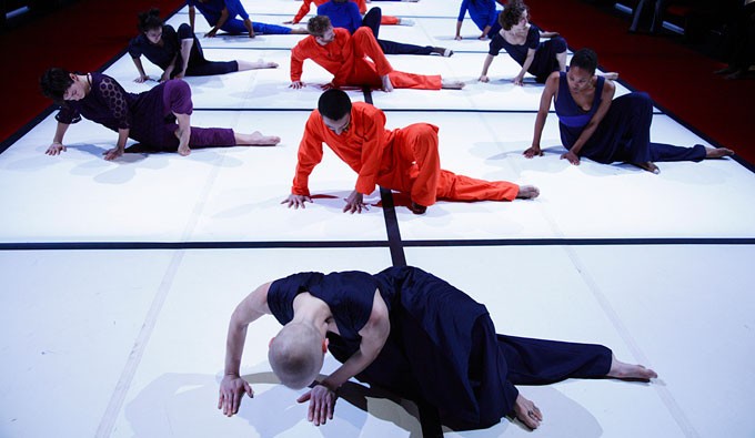 12 figures lay on the floor in nearly identical poses, both hands flat, right leg outstretched and left leg crossed over 