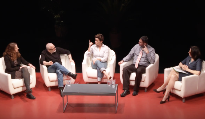Two white-cis men sit in white chairs on either side of a white-cis woman in a chair who is speaking in American Sign Language