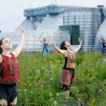 Dancers looking to the skies, standing an a wildflower meadow rooftop, a steal plant in the backgroun, hands open to the skies