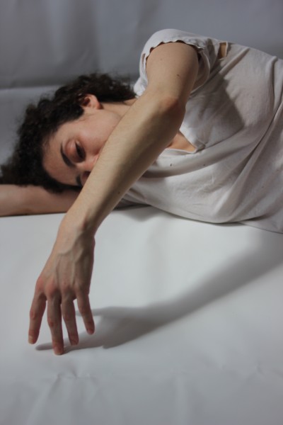 Person in white tee-shirt lies on her right arm on her side tracing the floor with the fingertips of her left hand 