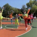Dancers in brightly colored neon outfits performing a ballet piece on an outdoor track
