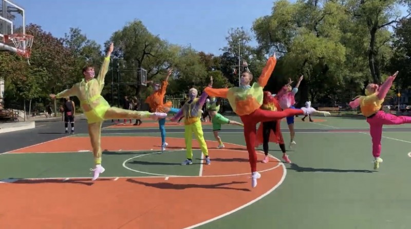 Dancers in brightly colored neon outfits performing a ballet piece on an outdoor track