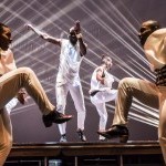 Dancers of Step Afrika! dressed in all white costumes with light streams behind