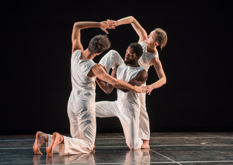 Dancers of Trisha Brown Dance Company in a gentle entanglement with two of the three dancers kneeling