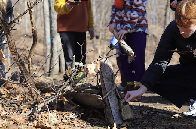 A piece of wood rests on a log with BDT company member Sean holding a small piece of moss next to it.  