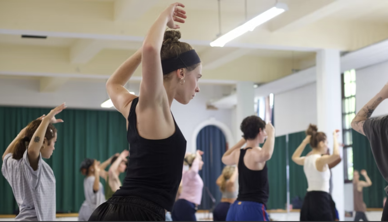 2024 SIP participant Leslie stands facing right with their arms up.