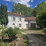 Photo shows a quaint French house surrounded by trees with a path leading up to it. 