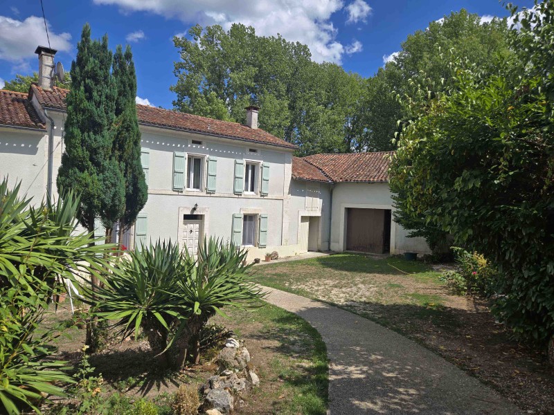 Photo shows a quaint French house surrounded by trees with a path leading up to it. 