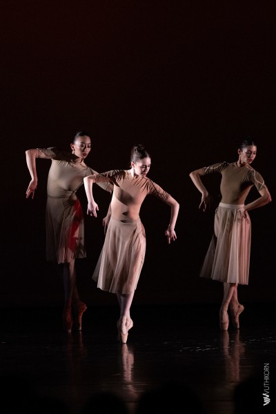 In front of an orange backdrop, a male dancer lifts another dancer high above his head