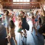 An image of adults and children dancing in a studio with mirrors together. 