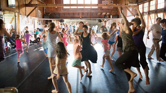 An image of adults and children dancing in a studio with mirrors together. 