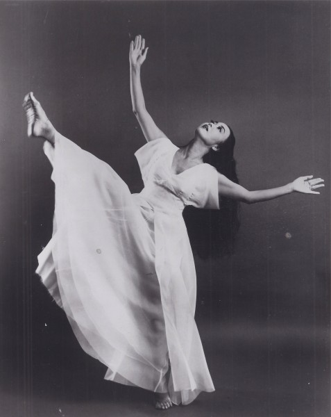 Image of Yuriko dancing in a light garment with arms reaching and leg extended