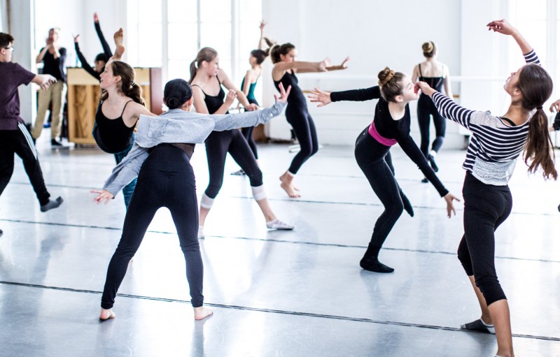 Many young dancers in a bright studio dancing contemporary movement.
