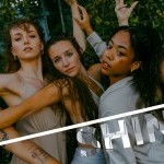 5 female dancers posing towards the camera closely infront of a green vine wall