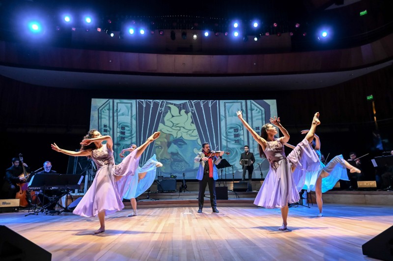 violinist center stage, surrounded by 4 dancers in blue and purple dresses