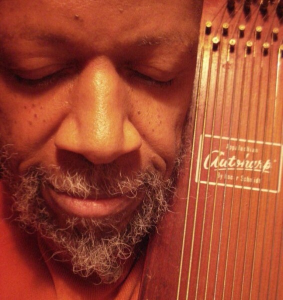 Close up of Laraaji with his eyes closed, holding his zither. 