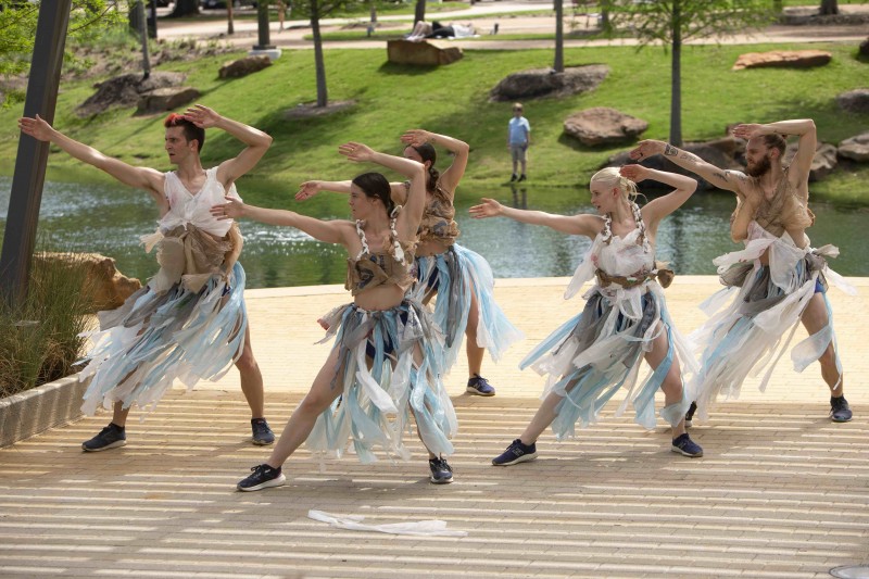 A photo of five dancers wearing costumes made of recycled plastic bags. They all lunge in one direction with their arms up.