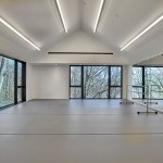 A brightly lit dance studio with grey marley floors, a mirrored walls and two large windows looking into a forest.