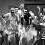 A group of dancers stand in a clump with happy expressions across their faces