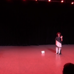 raha and zav&eacute; wear black and white tunics and stand with arms raised in a pink-lit space with a white Rangda mask between them.