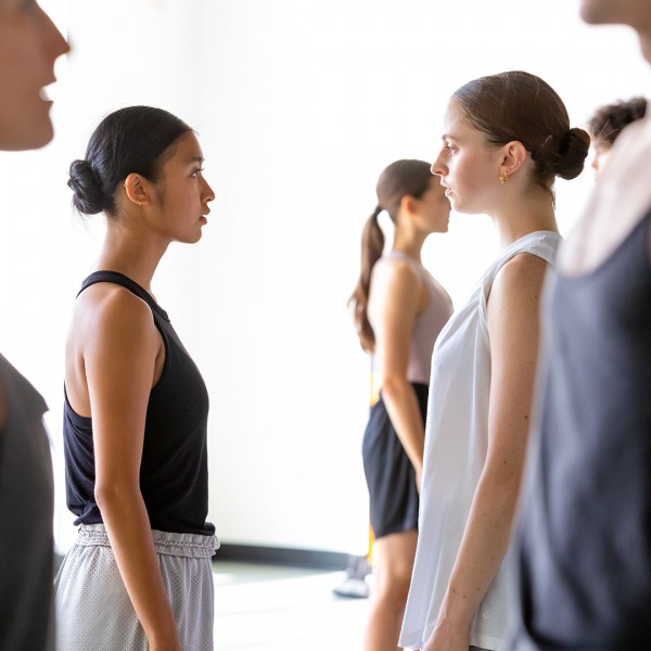 Two dancers stand facing each other in a light-filled studio