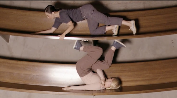 Two dancers are climbing on wooden pews. 