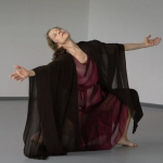 dancer kneeling with open arms, head tilted back costumed in flowing robes