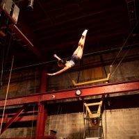 An acrobat flies through the air reaching for the trapeze bar.