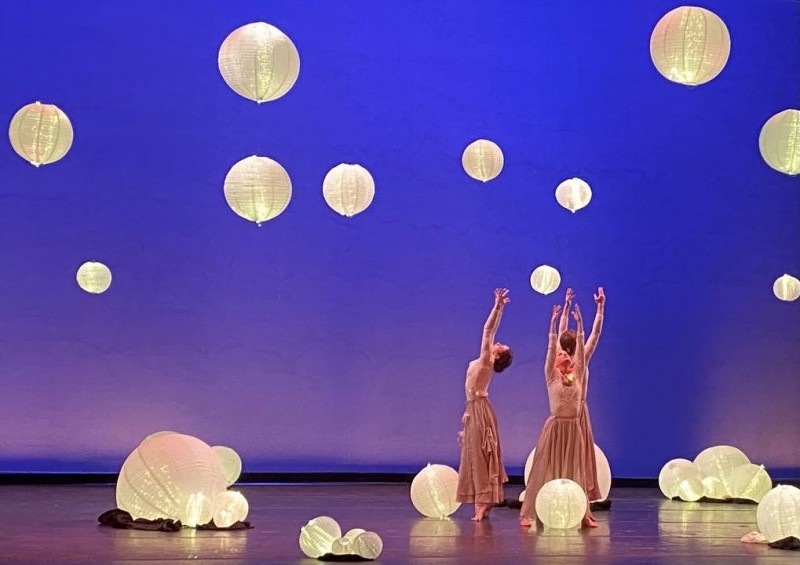 Dancers stand with arms raised overhead with a purple backdrop and illuminated lanterns surrounding them.