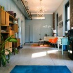 Photo of large lobby with light blue walls and large windows. There are lots of plants around and two colorful carpets.