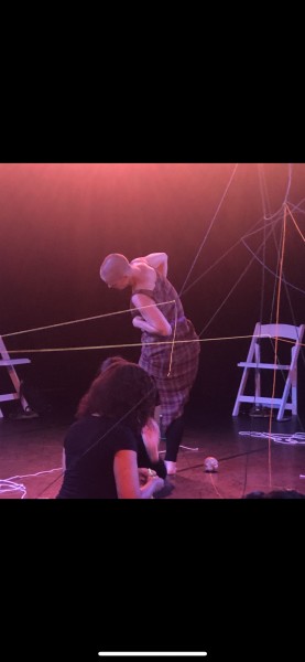 A performer in a dress leaning to the left amongst strings hanging from all angles. 