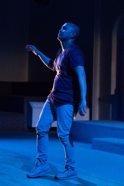 A performer wearing a maroon colored shirt and light pants. The performer is looking upward with their right arm lifted.