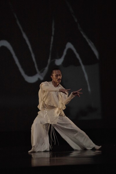 A dancer in white costume moving gracefully with detailed hand gestures