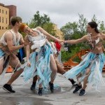 Three dancers in costumes made of recycled plastic bags perform in an outdoor urban environment.