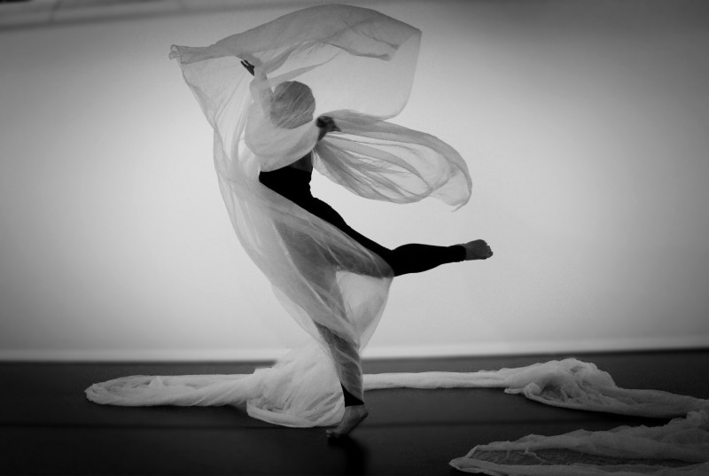 Dancer in arabesque with soft white fabric floating and spiraling around the dancer