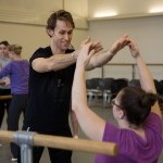 A NYCB artist leads a Workshop participant in movement at the barre.