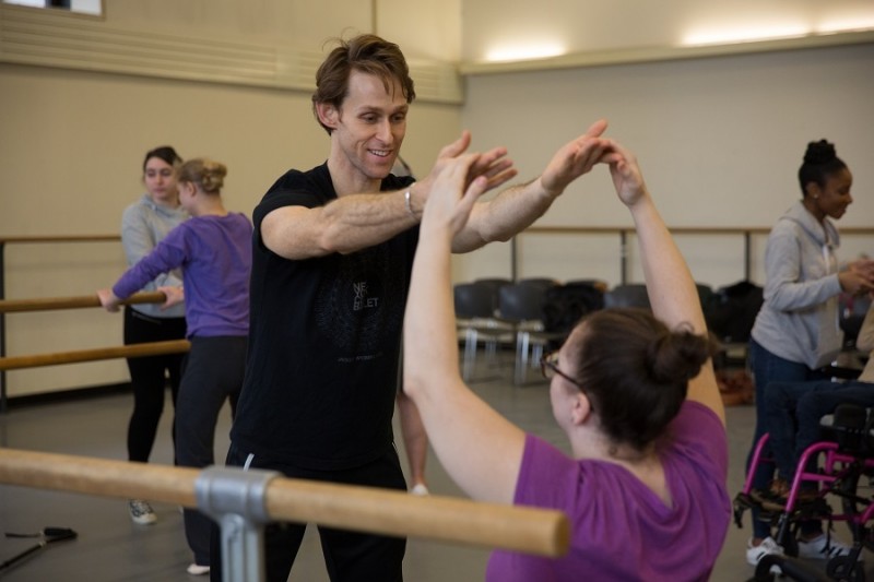 A NYCB artist leads a Workshop participant in movement at the barre.