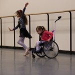 Two young dancers, one using a wheelchair, participate in a workshop.