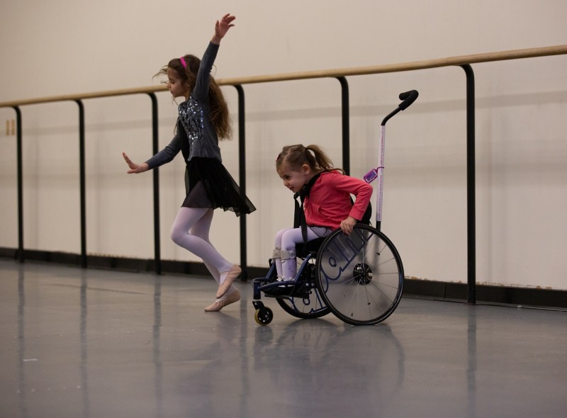 Two young dancers, one using a wheelchair, participate in a workshop.