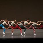 NYCB dancers in multi-colored tights stand on one bent knee, their other legs bent behind them and arms flexed.