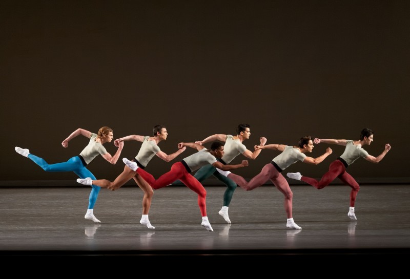 NYCB dancers in multi-colored tights stand on one bent knee, their other legs bent behind them and arms flexed.