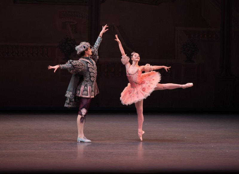 NYCB dancers perform a pas de deux. One dancer wears a pink tutu and the other wears a blue tunic.