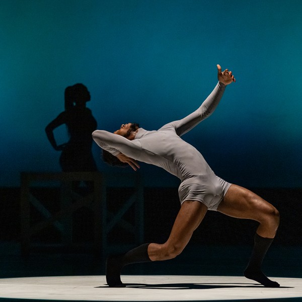 Black male dancer in deep lunch with back arched backwards on stage.