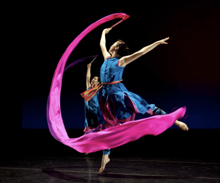 Two company dancers in blue costumes dancing with pink ribbon props