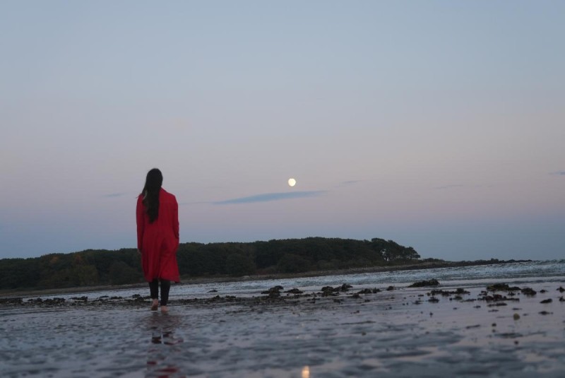 Nicole Canuso photographed walking on a beach at sunset in a red jacket