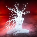 Vangeline performance photo - woman in white body paint with white tree branches on a red, ethereal backdrop